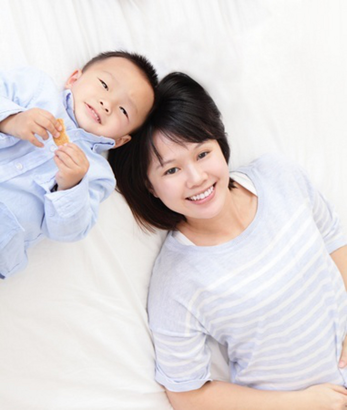 Happy cheerful mother and her pretty son lying on a bed